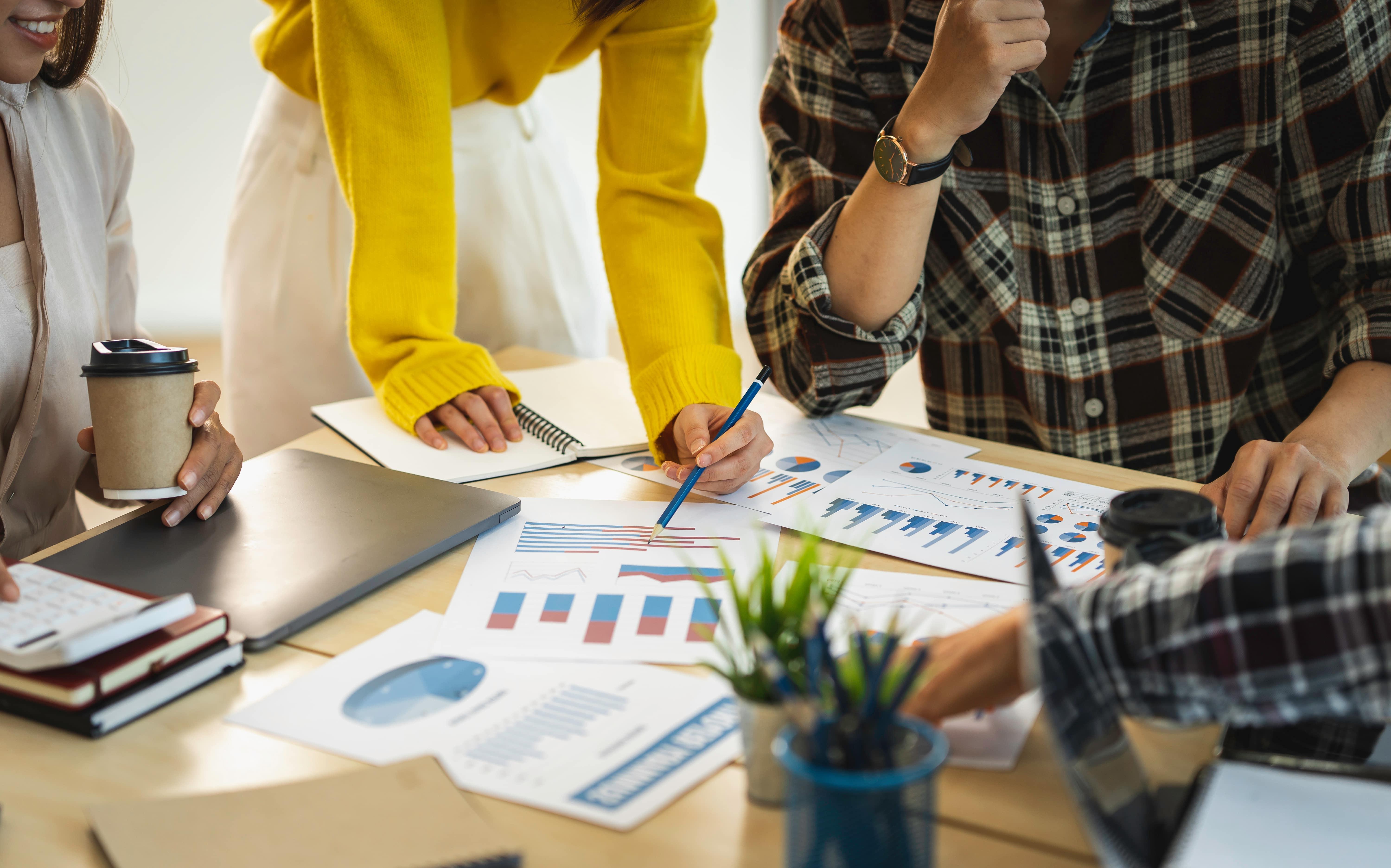 People sitting around a desk looking at several printed out graphs on the table.